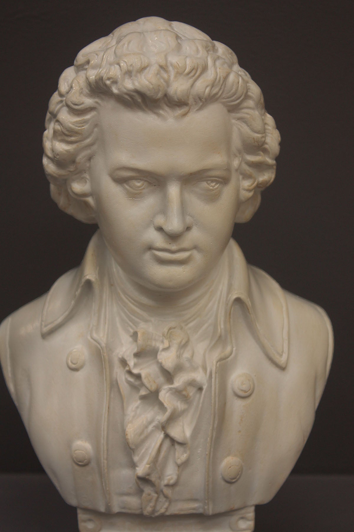 image of a plaster sculpture bust of man, namely Mozart, with ruffled necktie and coat on a gray background