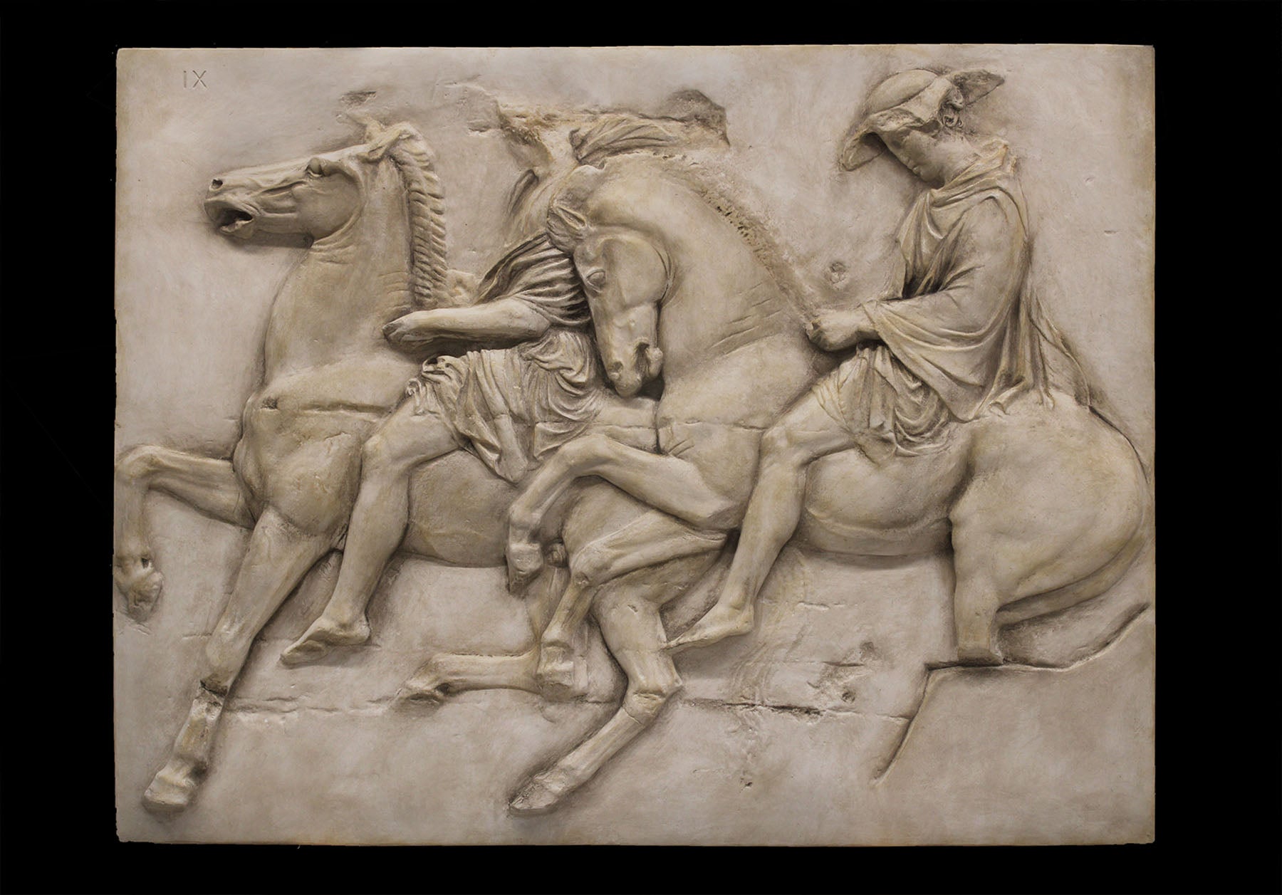 photo of off-white plaster cast relief sculpture of two men on horseback from Parthenon against black background