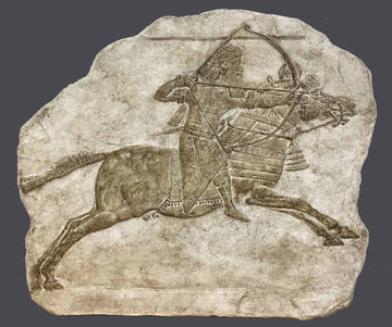photo of plaster cast relief sculpture of King Ashurbanipal on a horse and aiming an arrow in front of him with a gray background