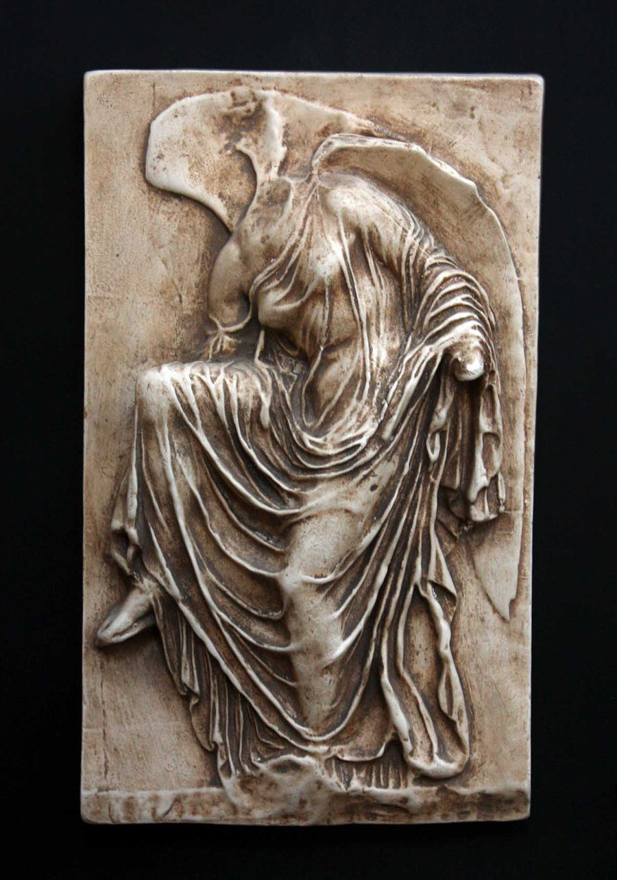 photo of cast of sculpture relief of robed figure, head now missing, reaching for her sandal in a brown patina on a dark gray background