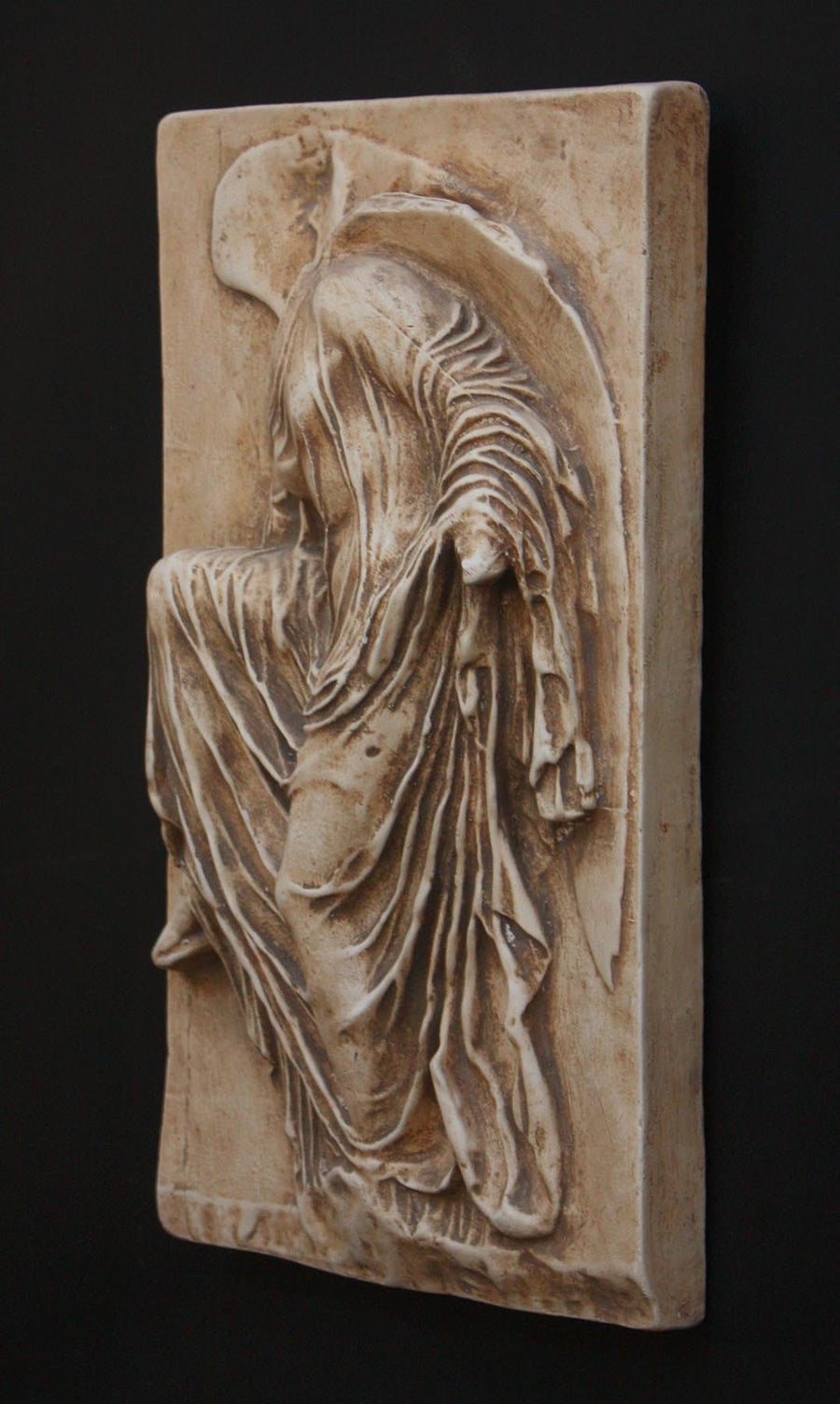 photo of cast of sculpture relief of robed figure, head now missing, reaching for her sandal in a brown patina on a dark gray background