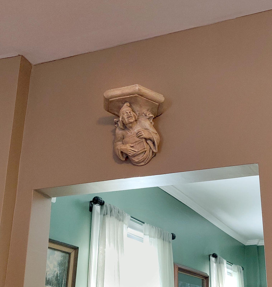 photo of plaster cast sculpture of architectural bracket featuring a man's upper body who holds a musical instrument, affixed to beige wall above doorway to room with green walls and curtains