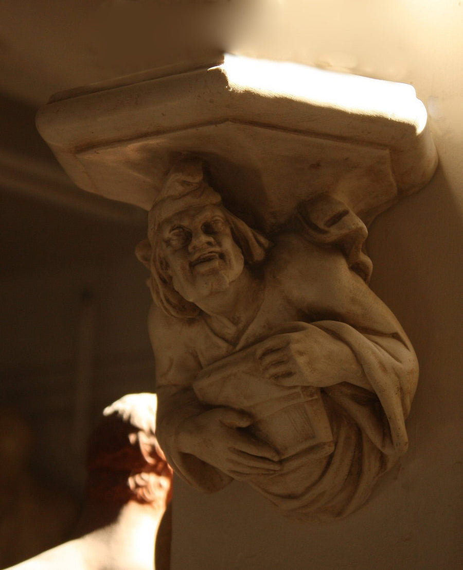 photo of plaster cast sculpture of architectural bracket featuring a man's upper body who holds a musical instrument and affixed to a beige column