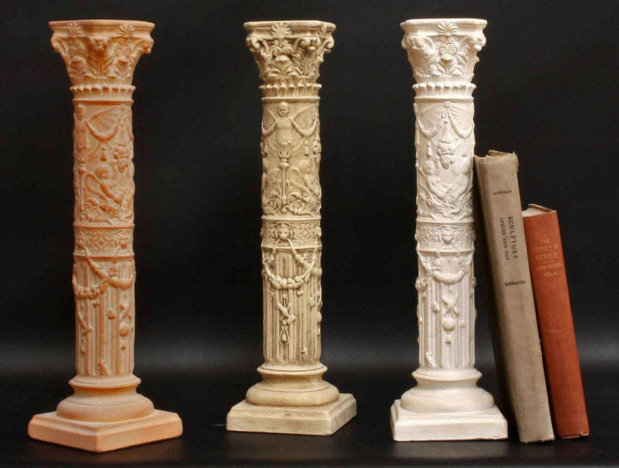 photo of three plaster casts of ornamental candlesticks in terra cotta, tan color, and ivory color and two books propped up against one with black background