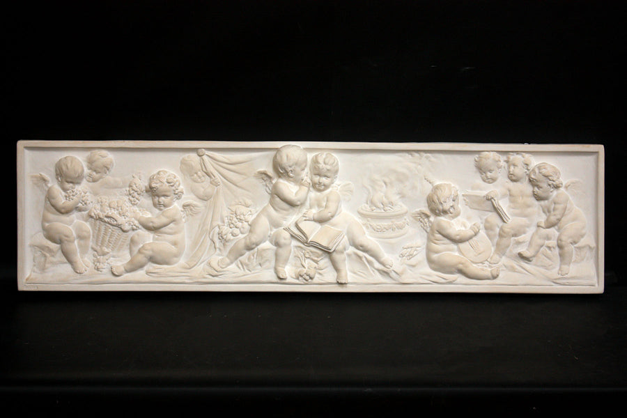 photo of white plaster cast with warm tones of relief sculpture of several cupids talking together with books and baskets of fruit on a black background