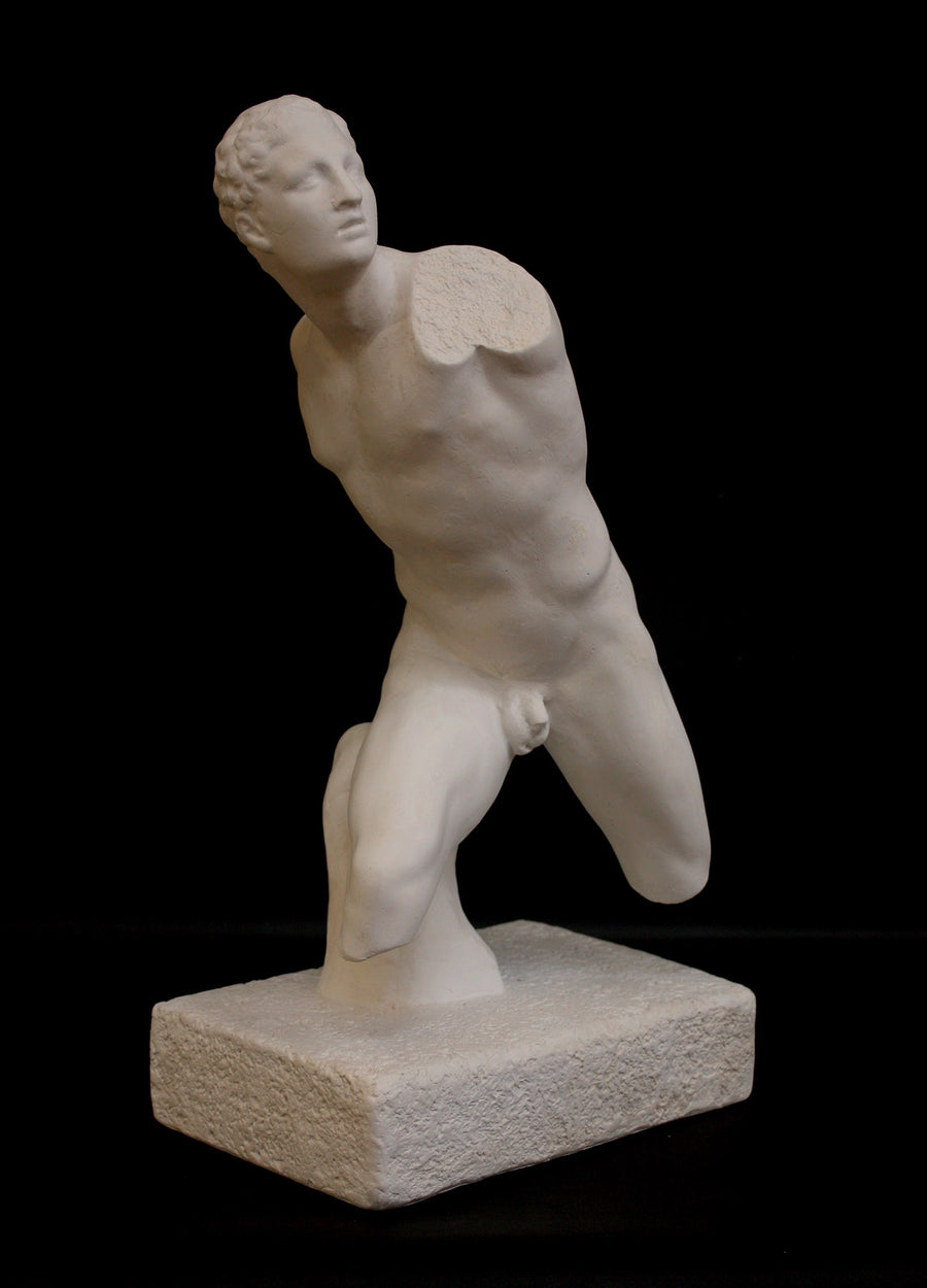 photo of white plaster cast sculpture of male figure in active pose without arms or lower legs on a base against black background