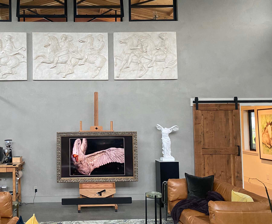 photo of white plaster cast sculpture of winged, headless female figure with flowing drapery against gray wall  beside swan photo and wood door and foreground with leather furniture