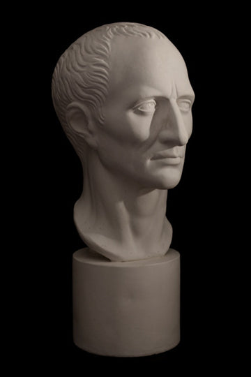 Photo with black background of plaster cast sculpture of man's head on cylindrical base