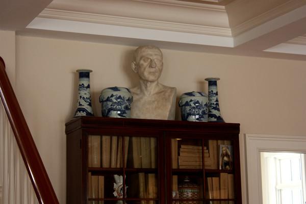 photo of plaster cast sculpture of male head of Cicero with squared bust and white and blue vases on a dark wood bookcase against a tan wall and staircase railing to the left