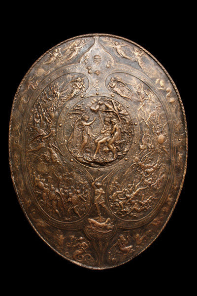 photo of bronze-colored plaster reproduction of a shield with intricate relief sculpture set against black background