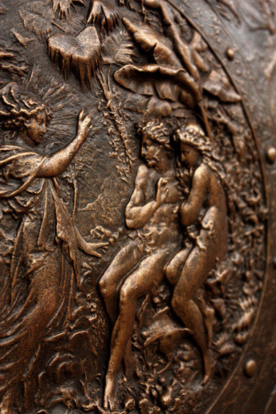 detail photo of bronze-colored plaster reproduction of a shield with intricate relief sculpture set against black background