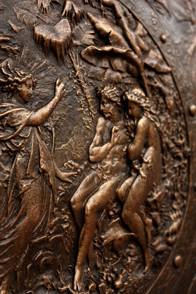 detail photo of bronze-colored plaster reproduction of a shield with intricate relief sculpture set against black background