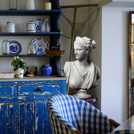 Photo of white plaster cast of sculpture bust of female goddess Diana with drapery and crown and up-do in a kitchen with blue hutch and chair