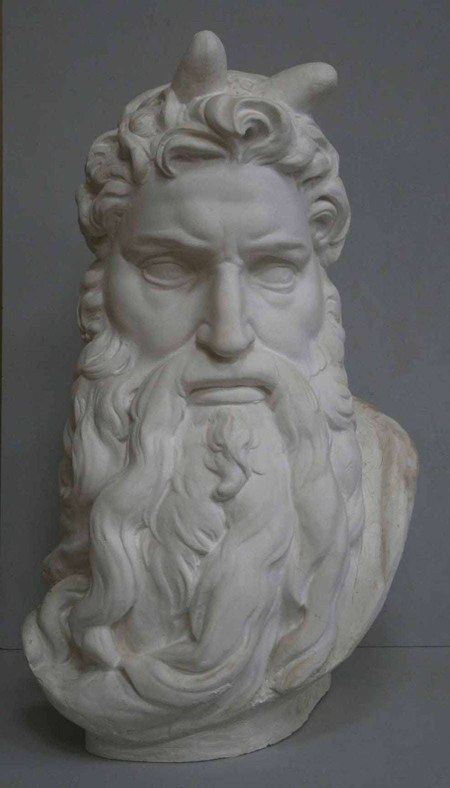 photo of plaster cast bust of man, namely Moses, with curly hair and so-called horns and long beard on gray background