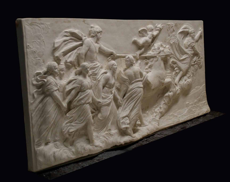 photo of a plaster cast sculpture relief of a woman, namely the goddess Aurora, flying and leading a chariot with a man pulled by horses towards the right while a cherub and other women fill the scene, on a black background