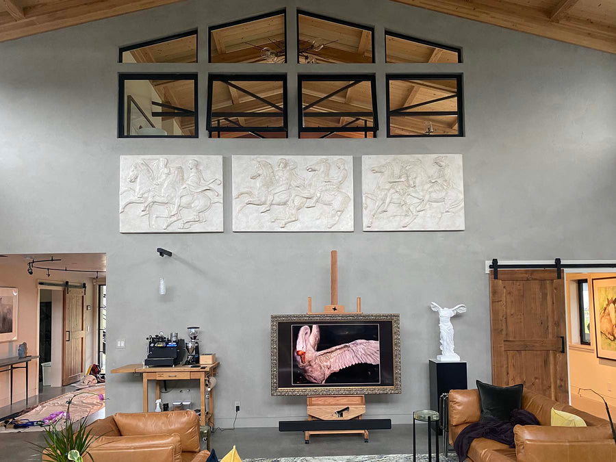 photo of row of three white plaster cast relief sculptures of men on horseback from Parthenon on gray wall under large windows and high ceiling with plaster cast statue of Victory of Samothrace and swan photo below