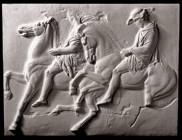 photo of off-white plaster cast relief sculpture of two men on horseback from Parthenon against black background