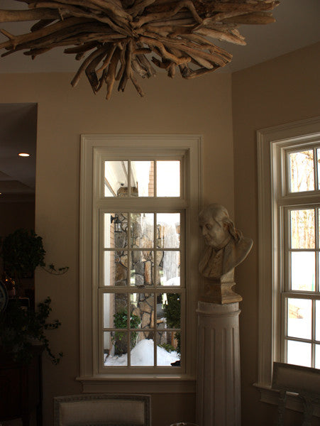 Photo of male bust sculpture on tall pedestal in between two windows in a dining room