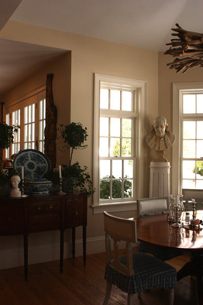 Photo of male bust sculpture on tall pedestal in between two windows in a dining room