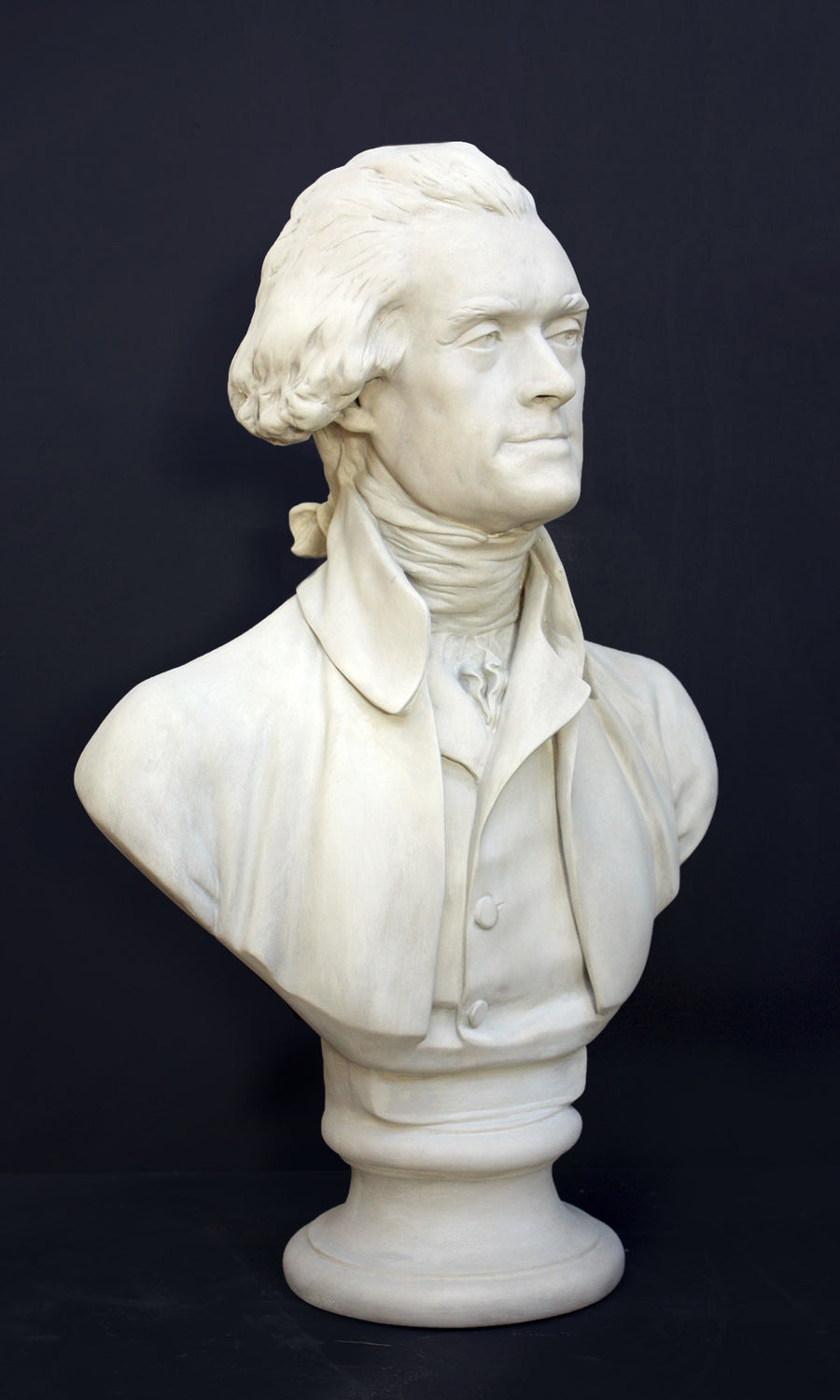 Photo of plaster cast bust sculpture of man with coat and neckerchief, namely Thomas Jefferson, with dark gray background