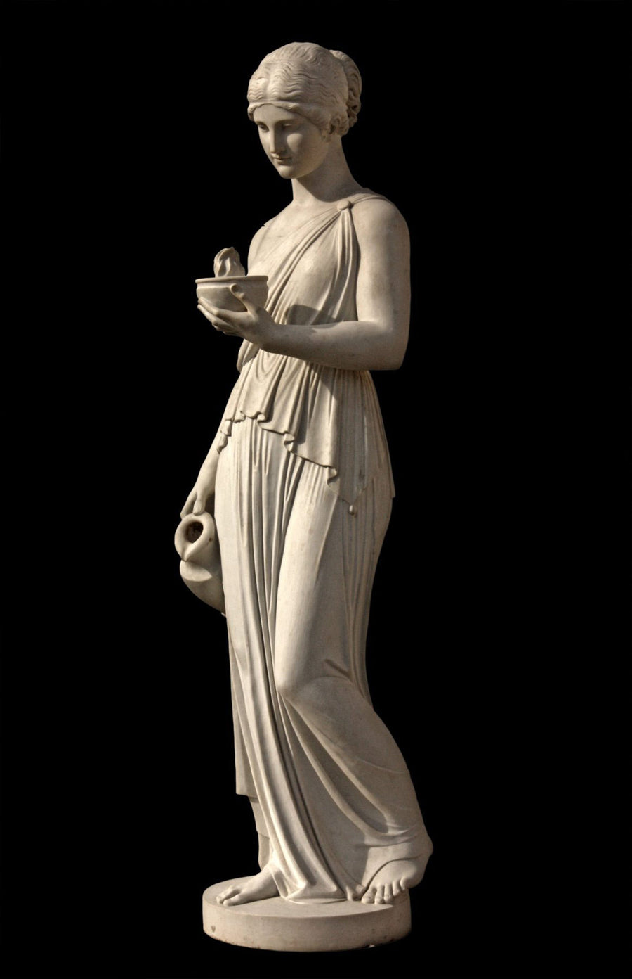 photo with black background of plaster cast sculpture of goddess Hebe in robes standing and holding a jug in right hand at her side and a bowl with a flame in left hand raised in front of her