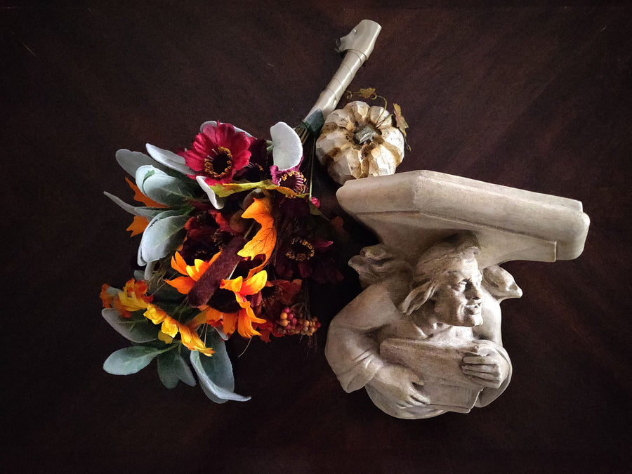 photo of plaster cast sculpture of architectural bracket on a dark table next to fall flowers and a pumpkin