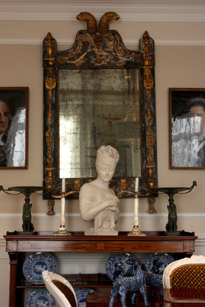 photo of plaster cast sculpture bust of Madame Recamier with high up-do and ribbon over forehead and hands crossed over chest covered in cloth on a dark wood table with bronze decorations, candlesticks, bronze framed mirror and two pictures, and blue and 
