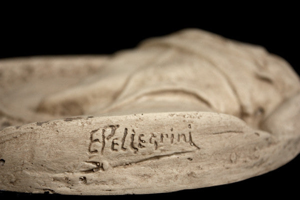 photo of plaster cast of small medallion with male portrait, view of bottom edge with artist signature on black background