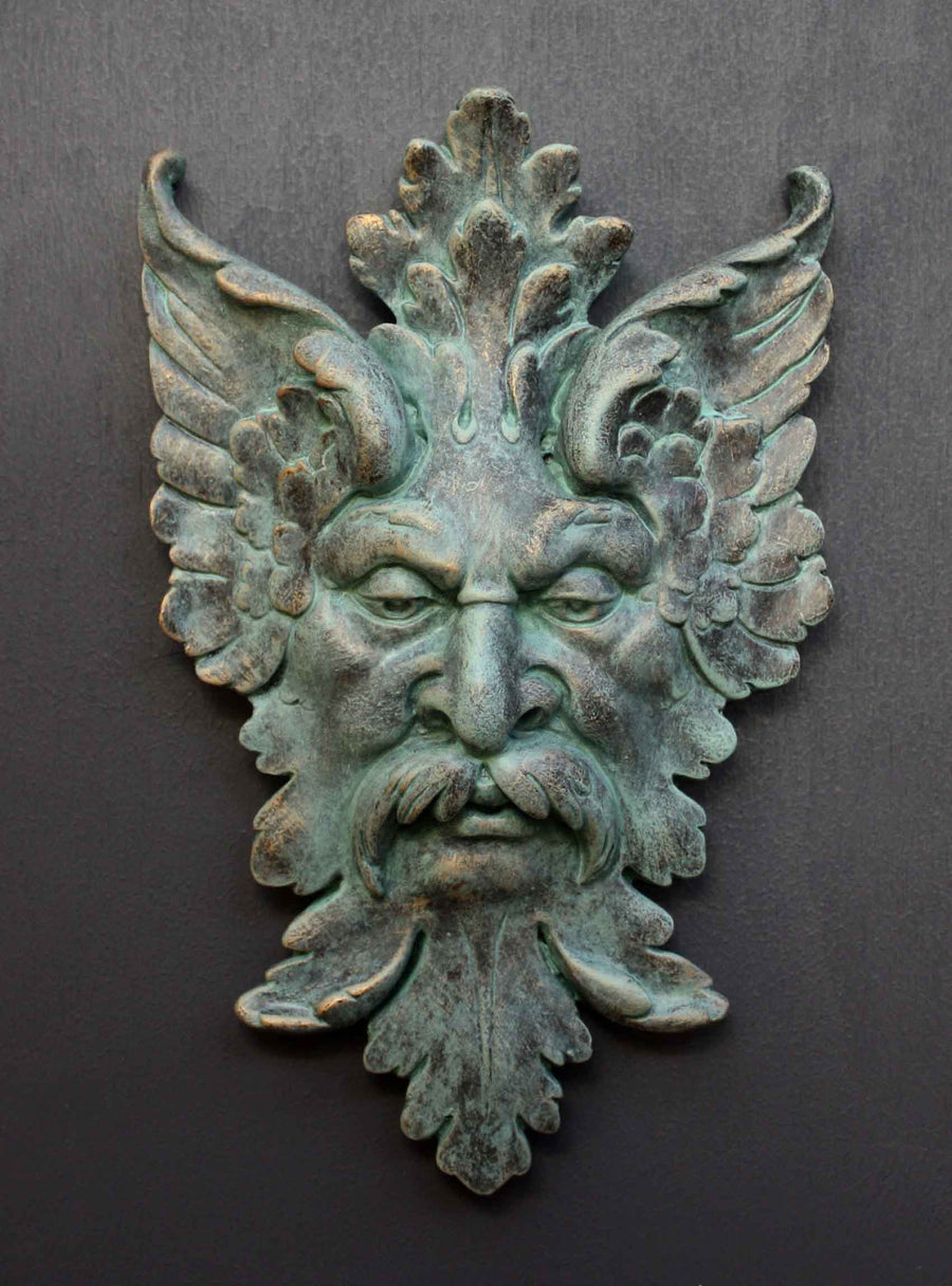 photo of verdigris-colored plaster cast sculpture relief of moustached man's face made of leaves with gray background