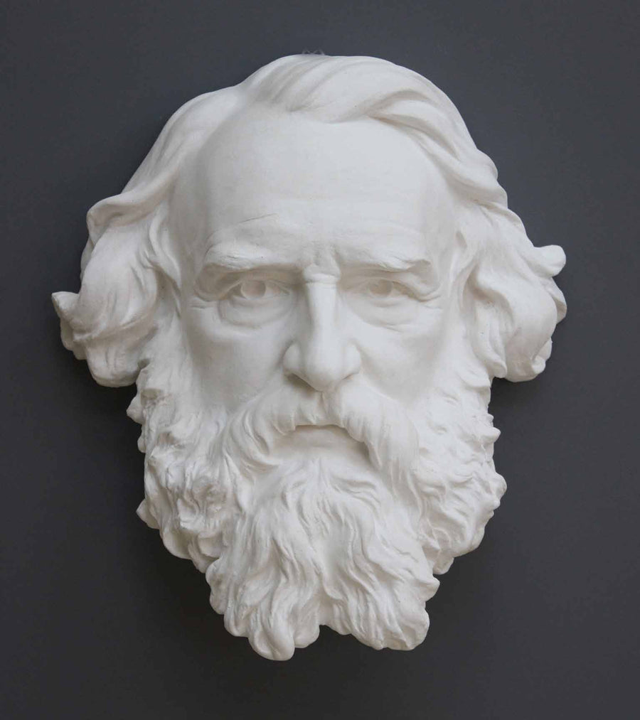 photo of plaster cast of man's head, namely Longfellow, with long hair and curly beard on gray background