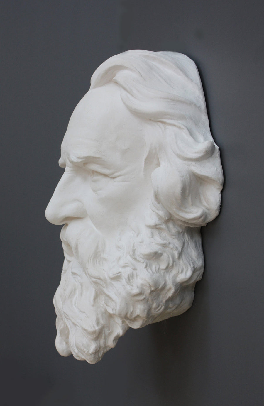 photo of plaster cast of man's head, namely Longfellow, with long hair and curly beard on gray background