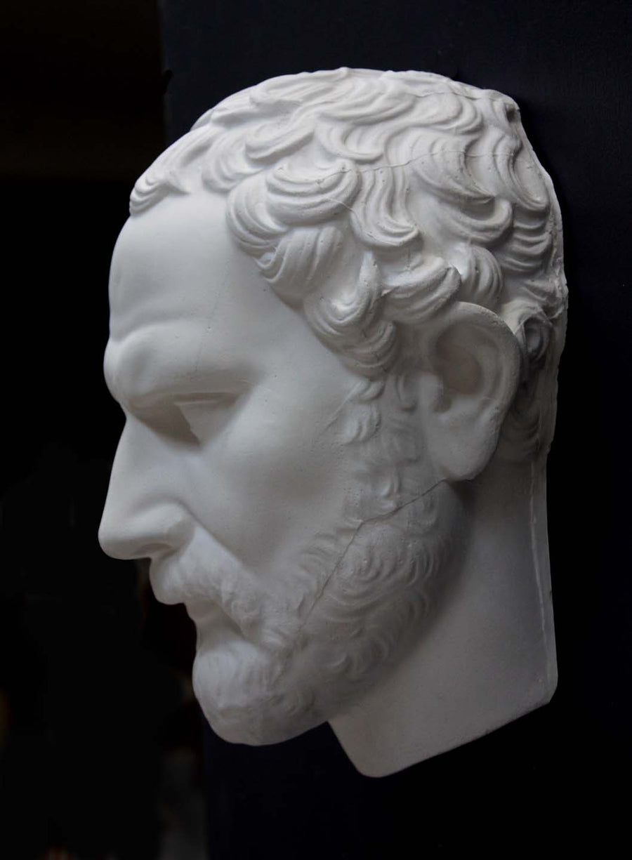 photo of white plaster cast of sculpture of face of Demosthenes with curly hair and beard on black background