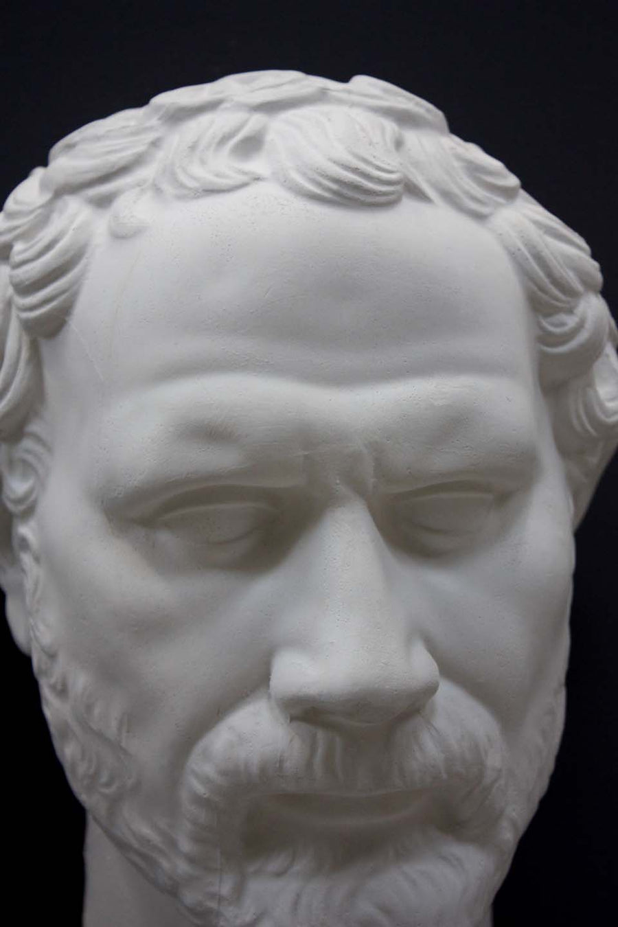 photo of white plaster cast of sculpture of face of Demosthenes with curly hair and beard on black background