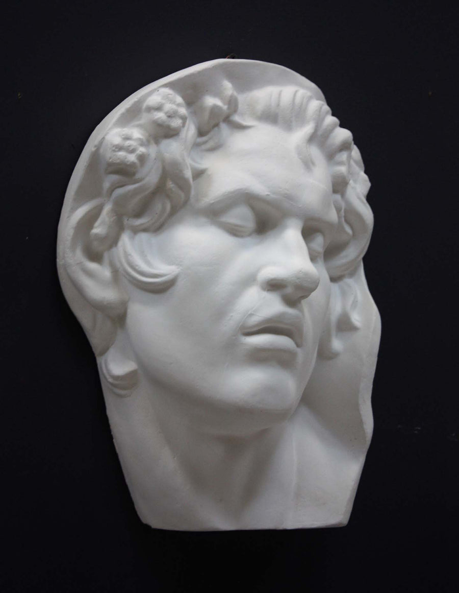 photo of plaster cast of sculpture of face of Sleeping Faun with two flowers in curly hair on dark gray background