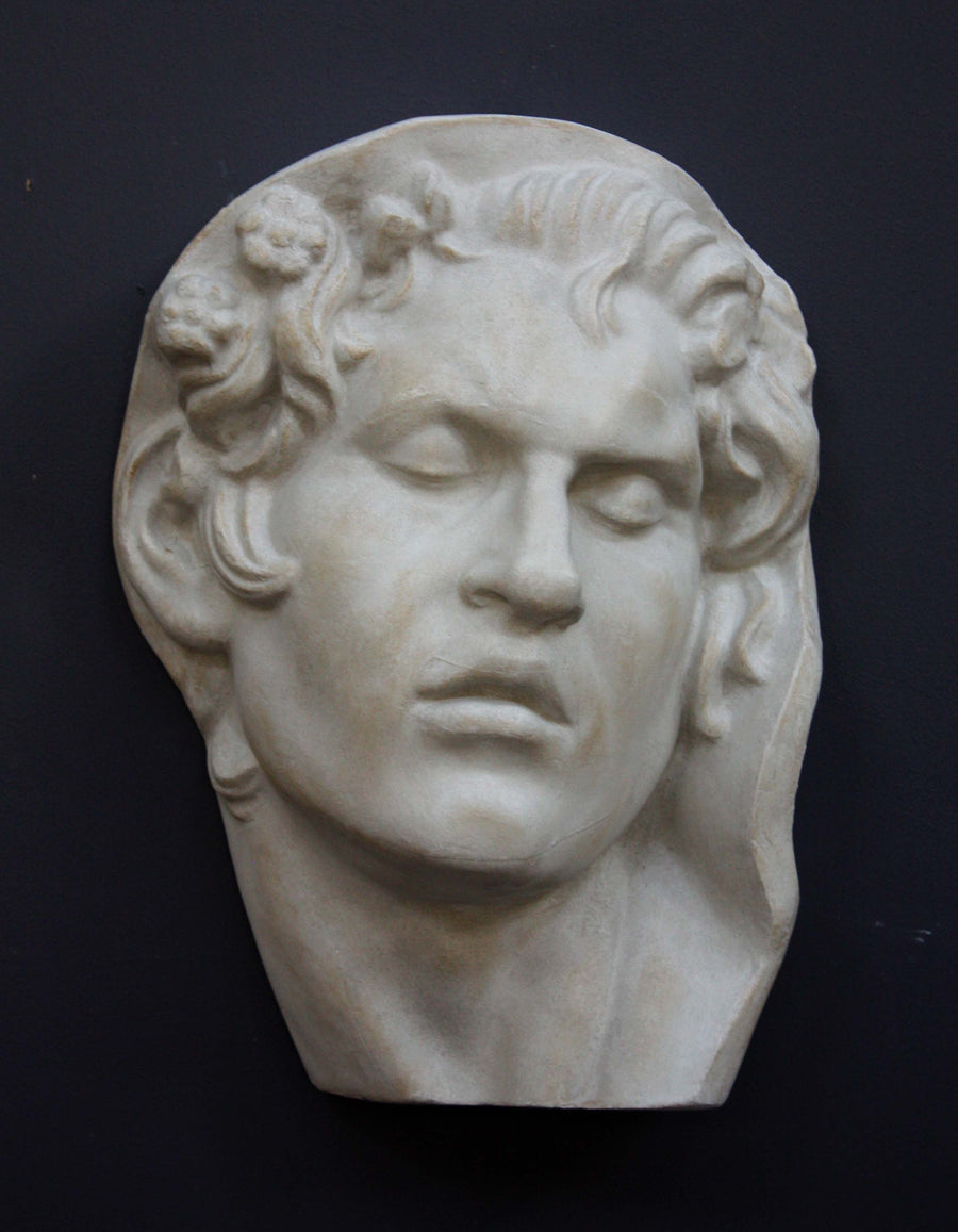 photo of plaster cast of sculpture of face of Sleeping Faun with two flowers in curly hair on dark gray background