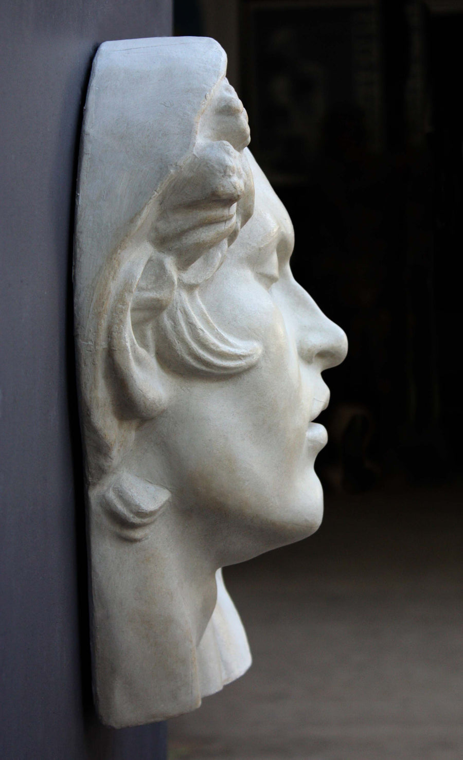 photo of plaster cast of sculpture of face of Sleeping Faun with two flowers in curly hair on dark gray background