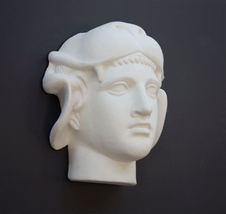 photo of white plaster cast of ancient sculpture of head, namely Omphale or Hercules, wearing Nemean lion skin against dark gray background