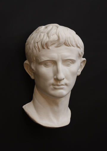 photo of white plaster cast sculpture of front half of head and neck of a male, namely Augustus Caesar, on black background