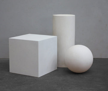 photo with grey background of plaster casts of three shapes arranged in a display- cube, sphere, cylinder
