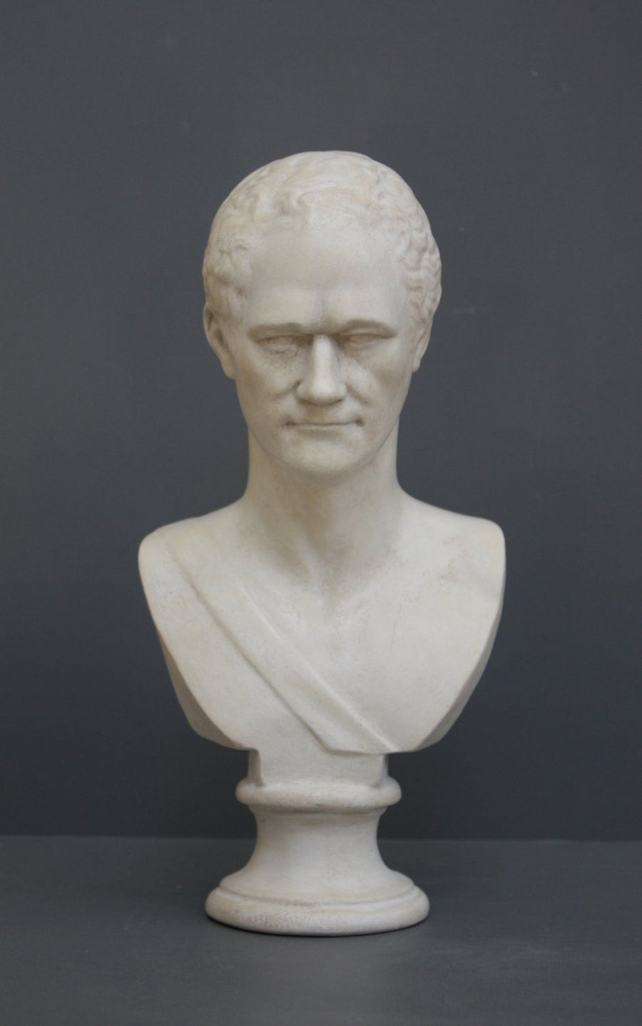 photo of white plaster cast bust of man, namely Alexander Hamilton, against gray background