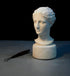 photo of plaster cast of ancient female bust, namely the goddess Diana, with a gray and black background and sculpting tool beside it