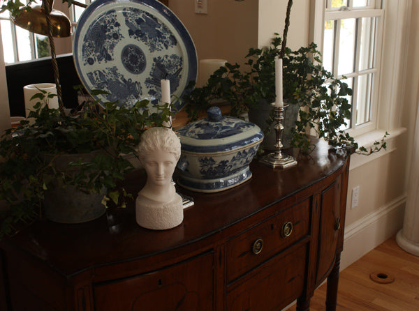 photo of plaster cast of ancient female bust, namely the goddess Diana, on a dark wood table with blue and white china and plants