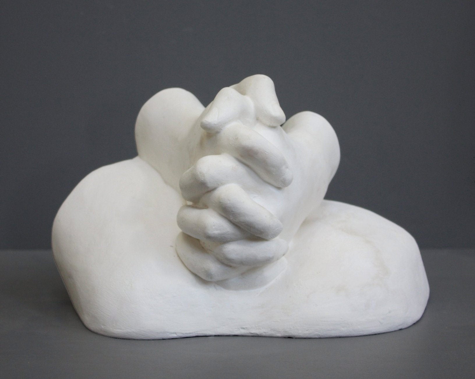 photo on gray background of plaster cast sculpture of Joan of Arc&#39;s hands clasped on top of a portion of her knees