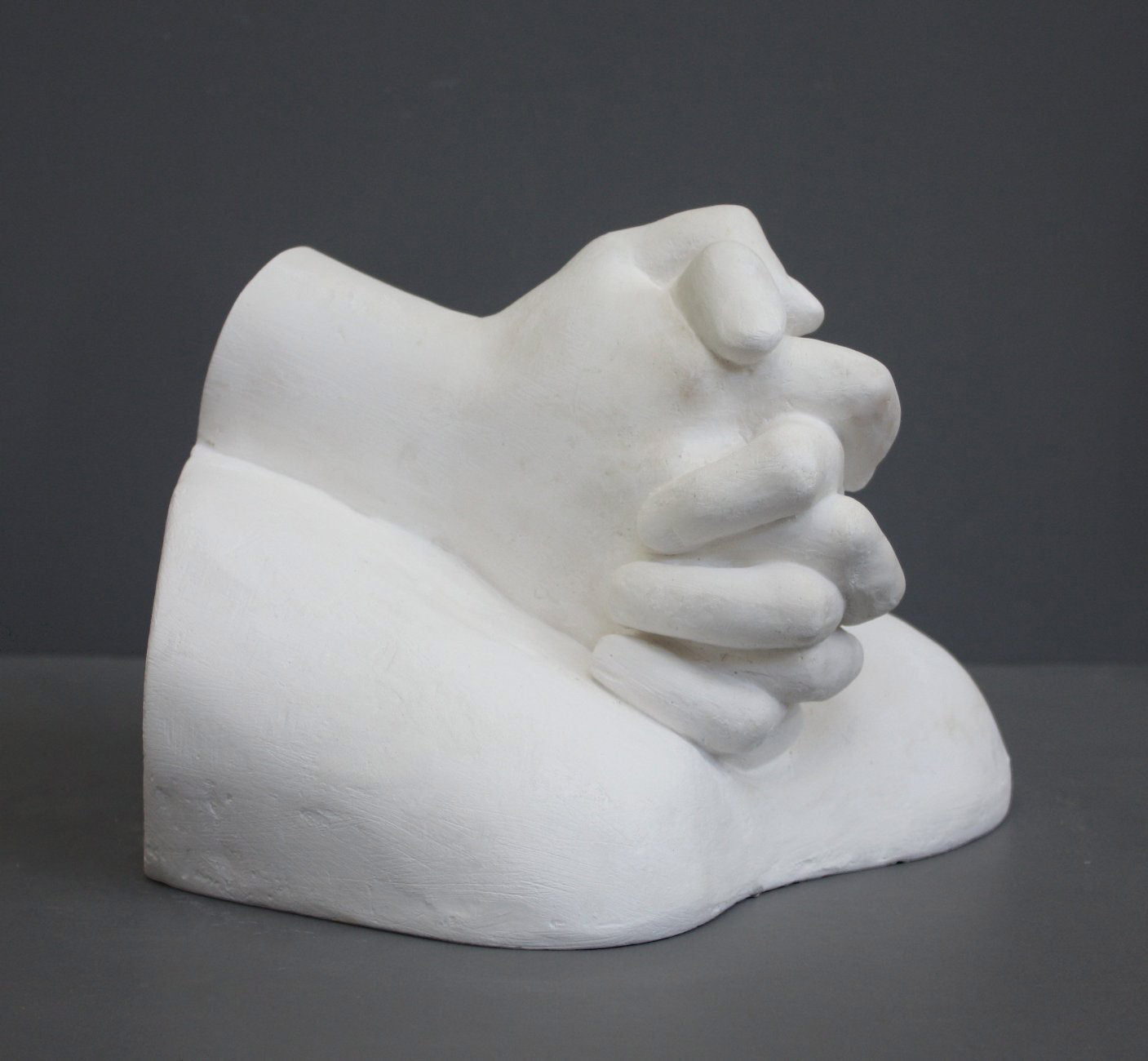 photo on gray background of plaster cast sculpture of Joan of Arc&#39;s hands clasped on top of a portion of her knees