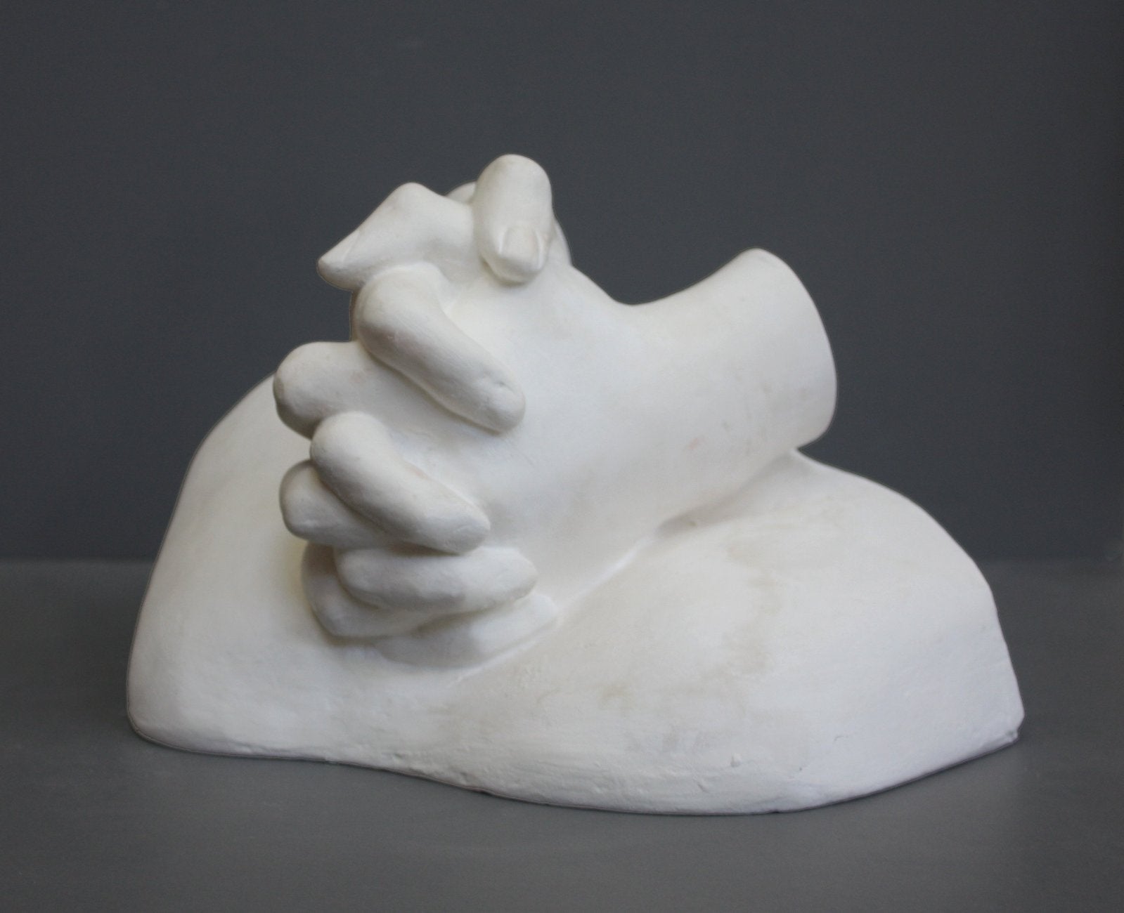photo on gray background of plaster cast sculpture of Joan of Arc&#39;s hands clasped on top of a portion of her knees