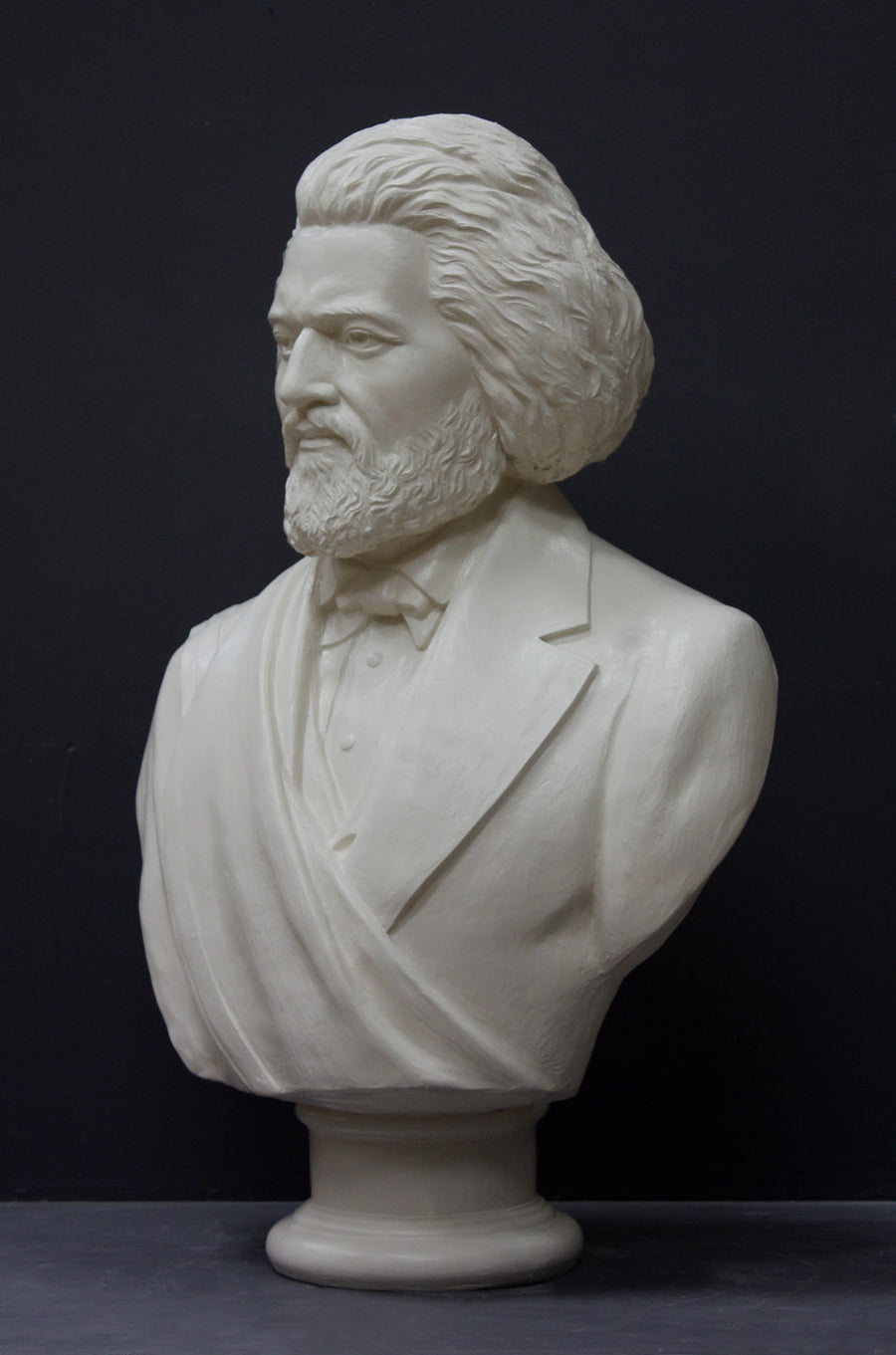 photo of white plaster cast sculpture of bust of Frederick Douglass with beard and in suit coat with toga over one shoulder on dark gray background