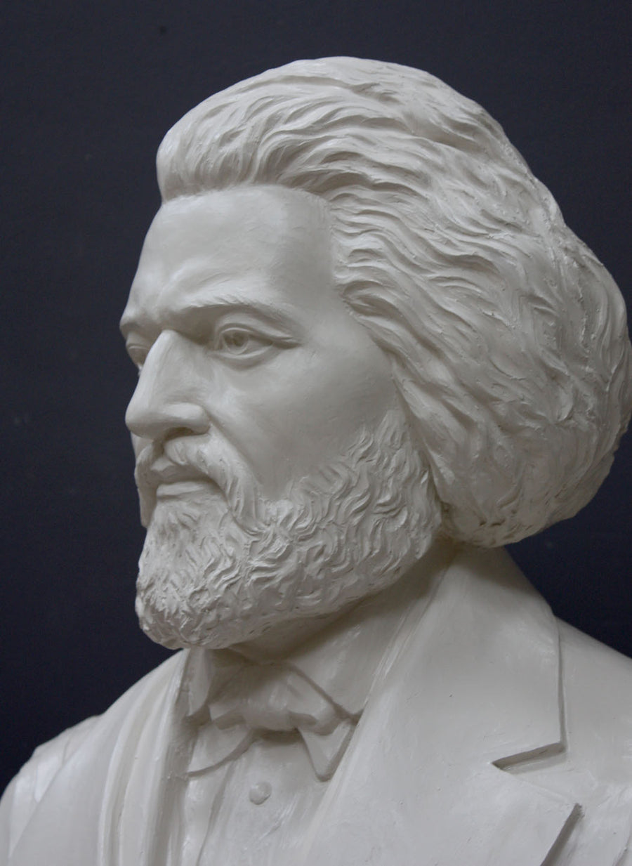 photo detail of white plaster cast sculpture of bust of Frederick Douglass with beard and in suit coat with toga over one shoulder on dark gray background