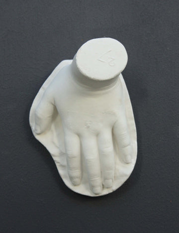 photo of white plaster cast sculpture of child hand against gray background