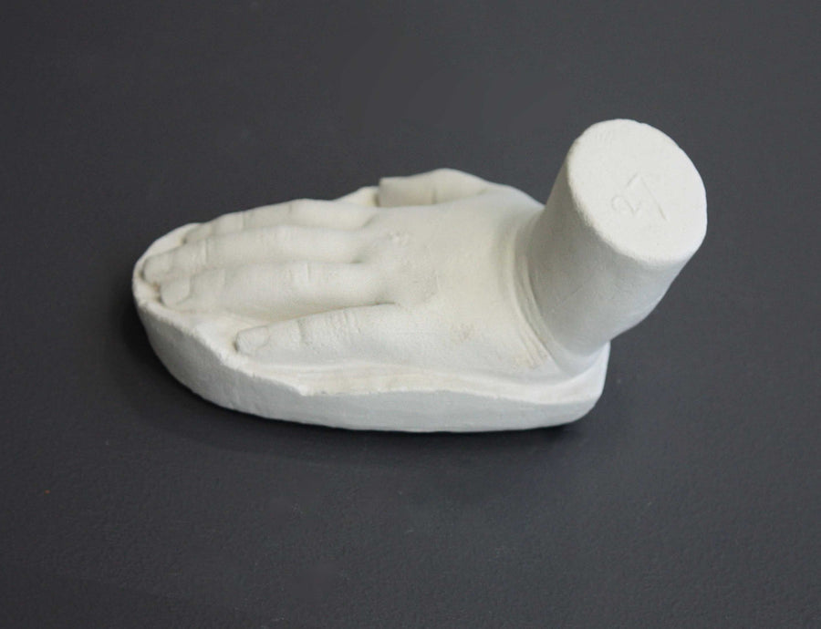 photo of white plaster cast sculpture of child hand against gray background