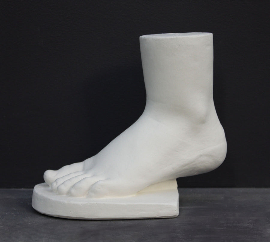 photo of white plaster cast sculpture of child foot against gray background